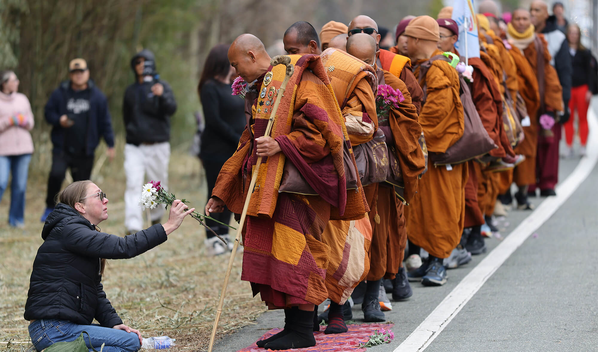 Monk accepting flowers from a woman during a peaceful Buddhist walk, illustrating the “let them” mindset of acceptance and inner peace.