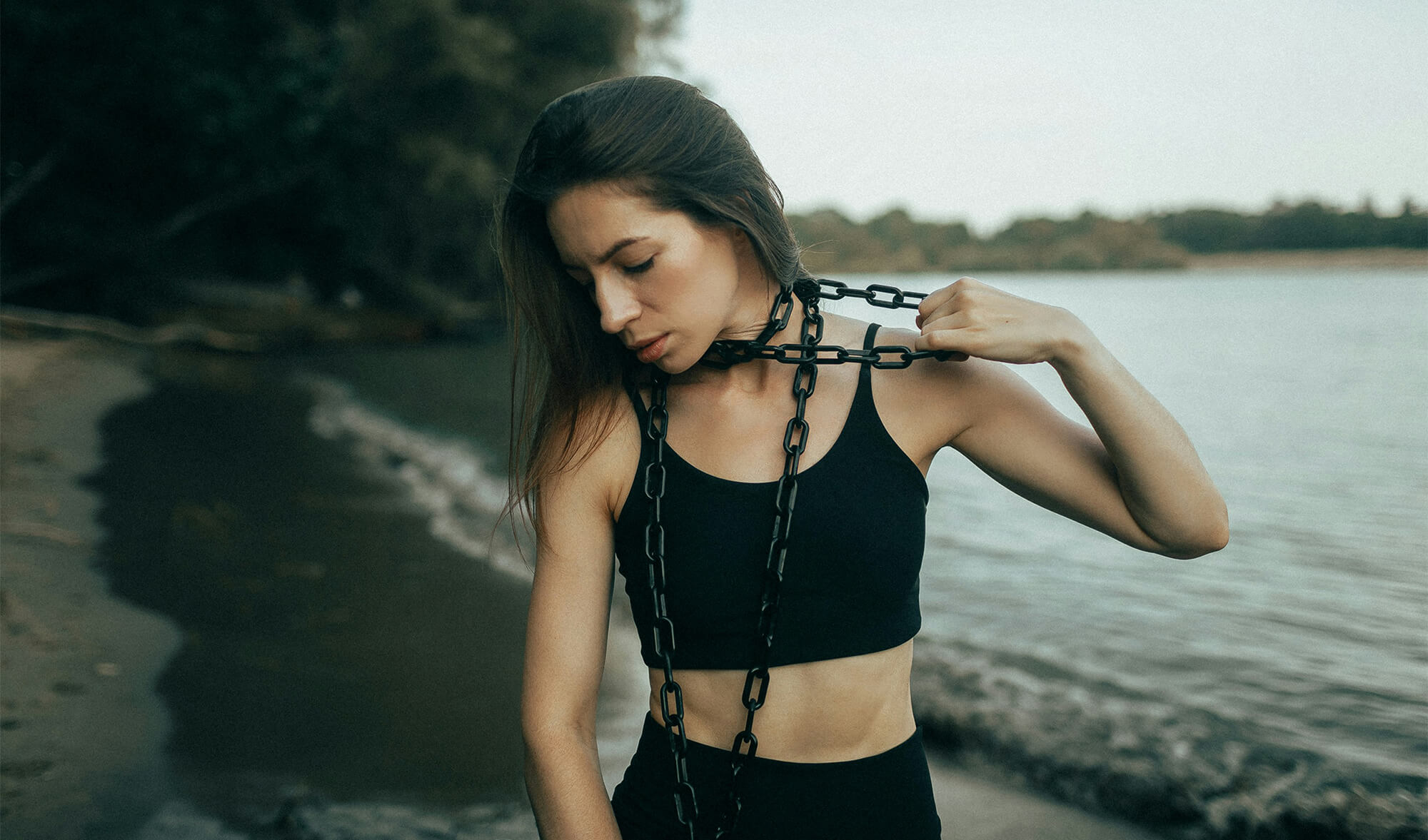 Woman wearing chains by the water, symbolizing the struggle of overcoming life’s challenges and feeling trapped.
